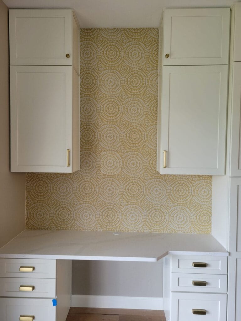 Office remodel featuring a custom built-in desk, cabinets, and stylish wallpaper for a functional and elegant workspace.