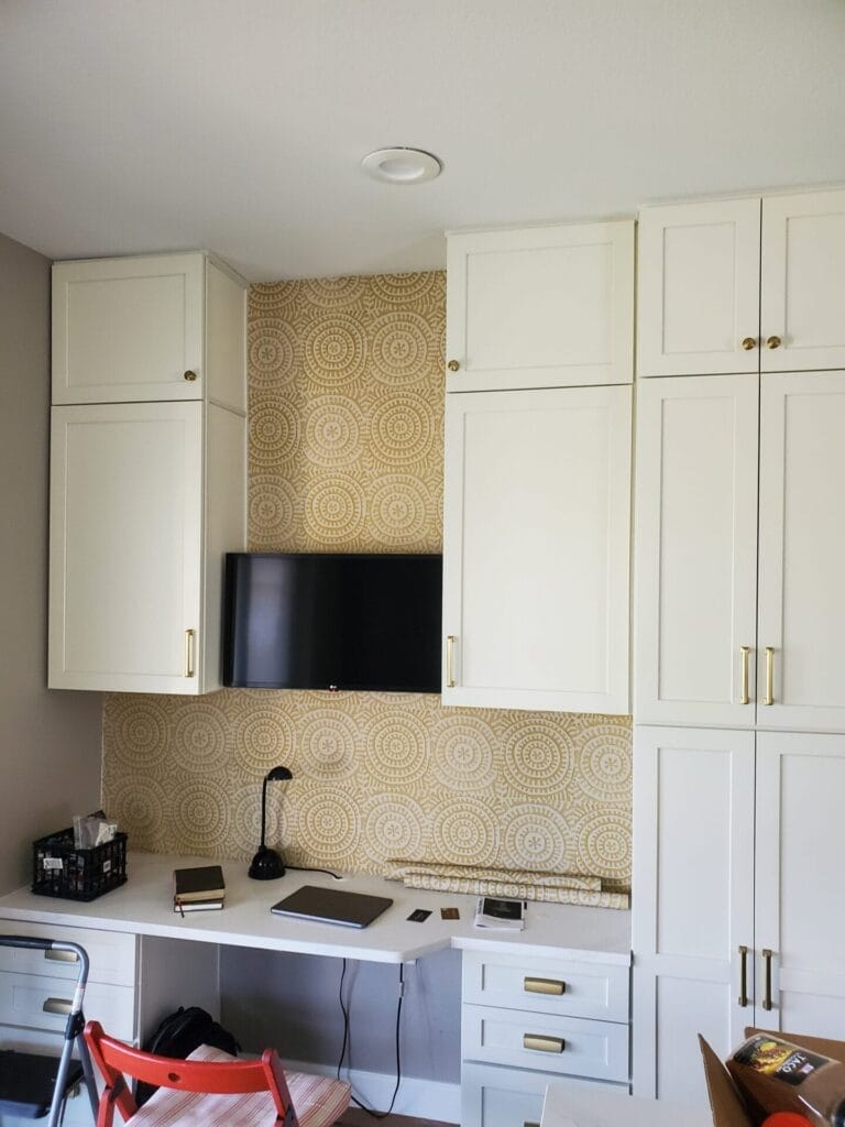 Office remodel featuring a custom built-in desk, cabinets, and stylish wallpaper for a functional and elegant workspace.
