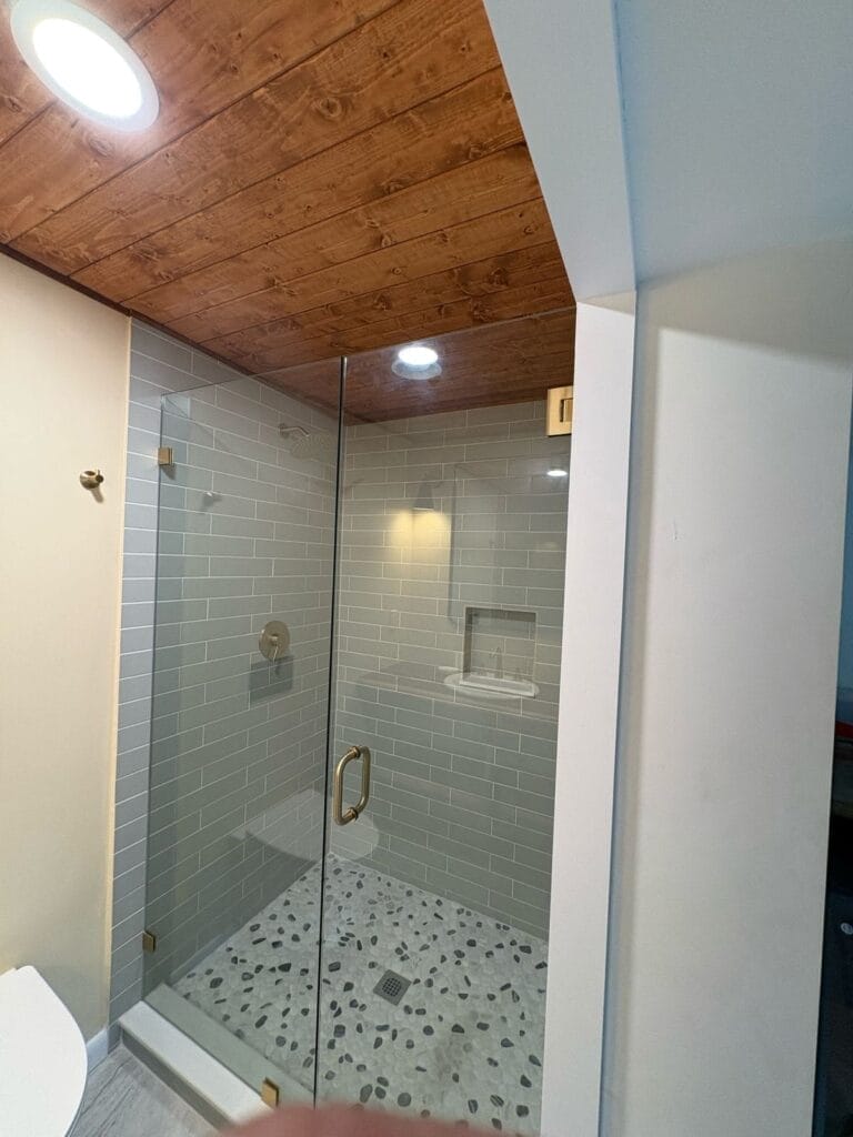 Walk-in shower with pebble tile floor, subway tile walls, and wood ceiling