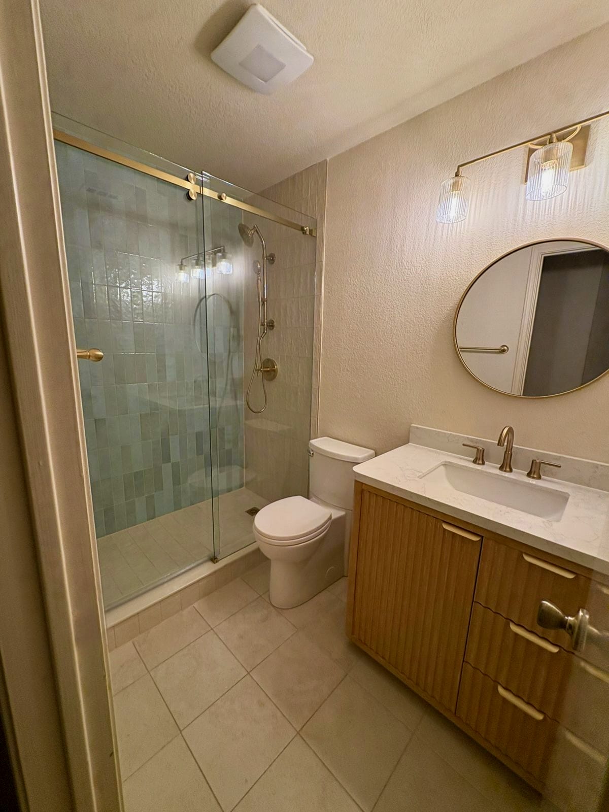 Full bathroom view showing sliding glass shower with sage tile, wood vanity, and gold fixtures