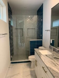 After: Modern bathroom with blue subway tile accent wall, gray shower tile, and new flooring
