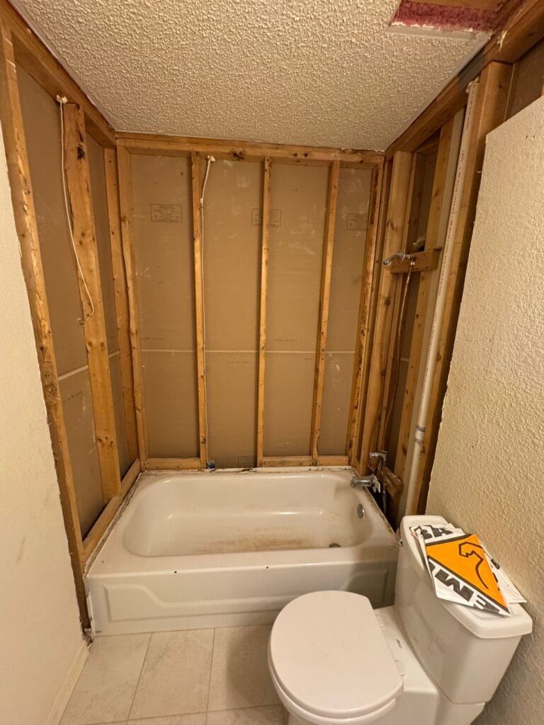 Bathroom during demolition showing exposed wall studs and old tub before shower conversion