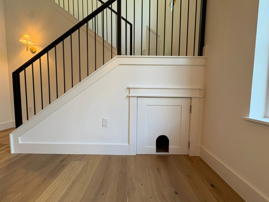 Finished under-stair cabinet with arched cat door opening and white trim work