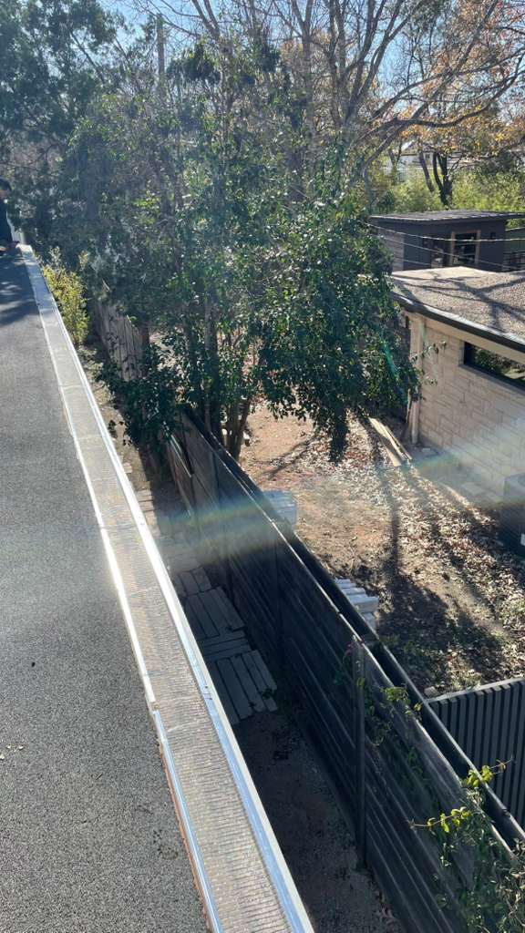 Long run of aluminum gutter guards on a flat roof section with mature trees overhanging nearby
