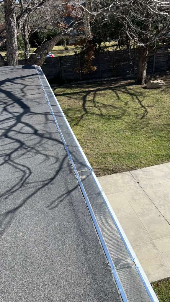Gutter guard installation wrapping around a corner near a window, with backyard and lawn visible below