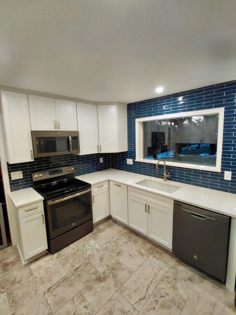 L-shaped kitchen after water damage renovation featuring white shaker cabinets, blue subway tile backsplash, quartz countertops, and natural light from window above sink