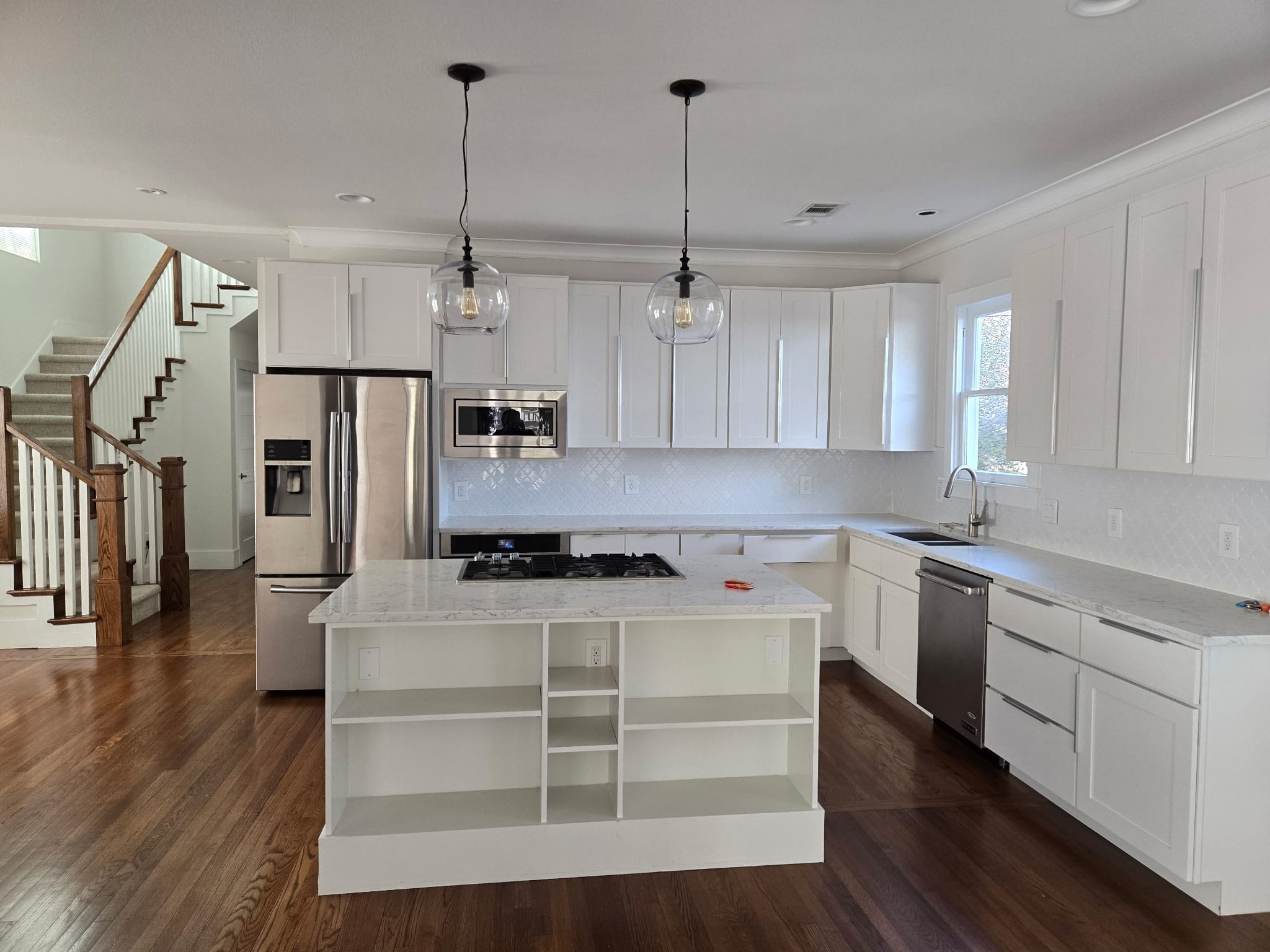 White shaker kitchen cabinets with marble countertops, center island with gas cooktop and open shelving, glass pendant lights, and stainless steel appliances