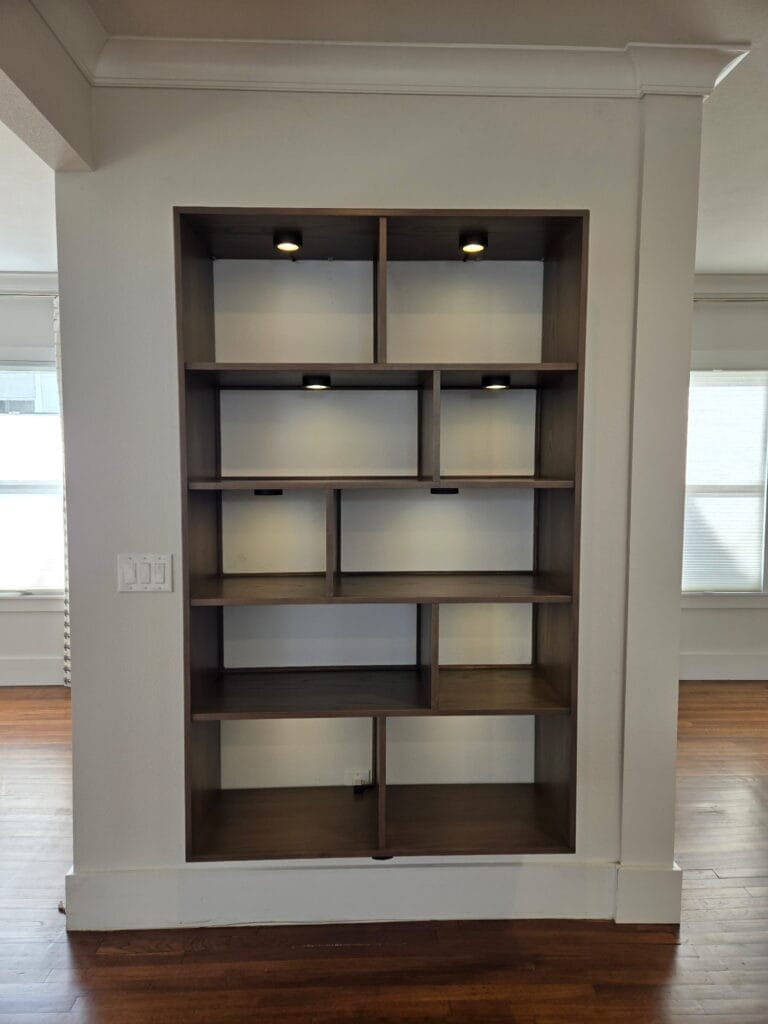 Custom built-in bookshelf with dark wood stain, asymmetrical shelf arrangement, and recessed puck lighting in wall niche