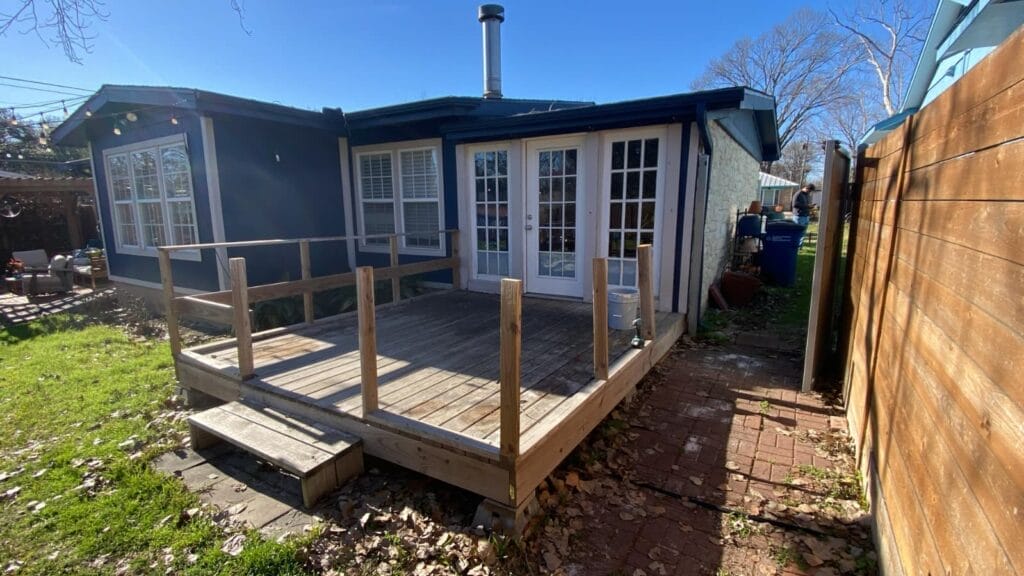 Old elevated deck with unfinished railing and weathered boards behind a blue home in Austin before removal
